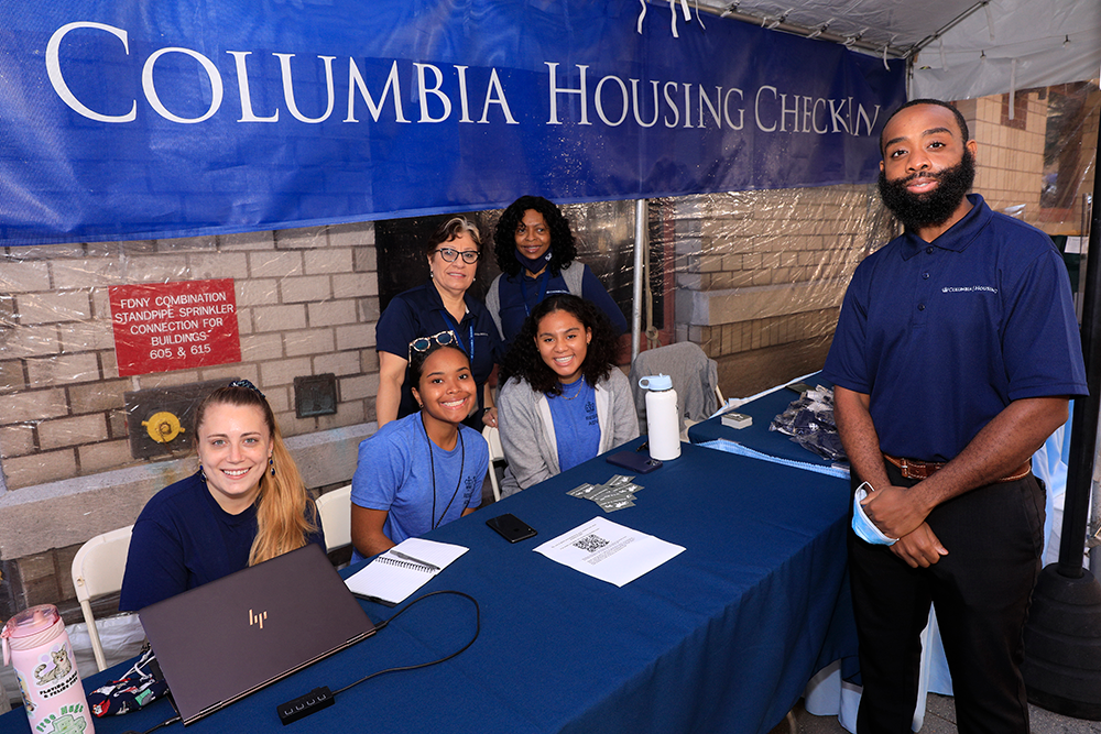 Housing staff stand under a Check-In tent