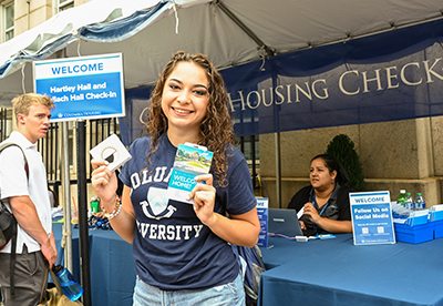 A student standing at a Check-In tent holding Check-In materials