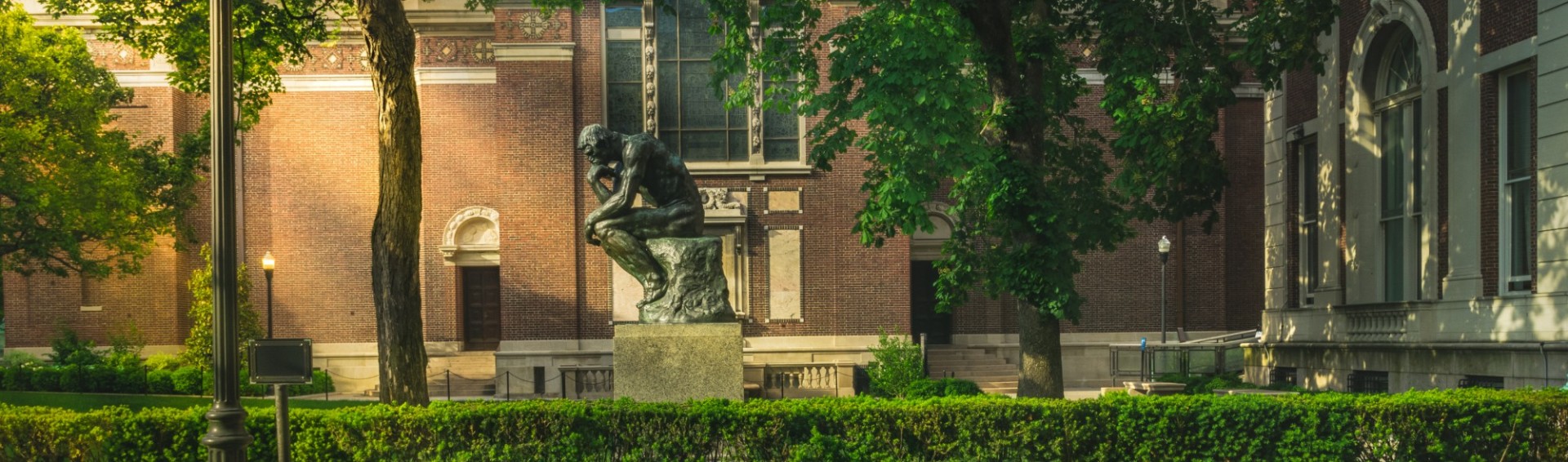 Auguste Rodin's sculpture The Thinker, sits in a sunlit lawn on Columbia University's campus.