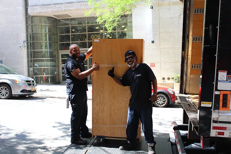 Two workers maneuver a wardrobe onto a truck