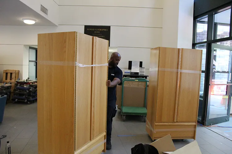 A worker wheels a wardrobe through the lobby of Schapiro Hall