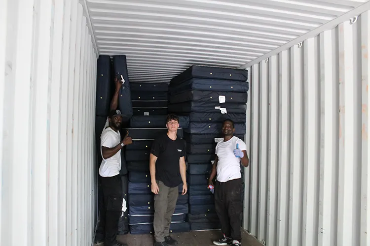 Three workers load mattresses into a truck