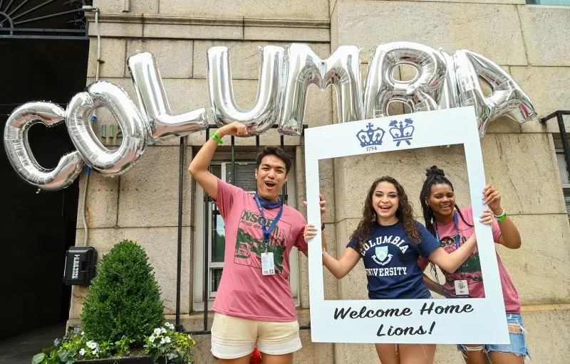 A new student and two orientation leaders under "Columbia" balloon letters
