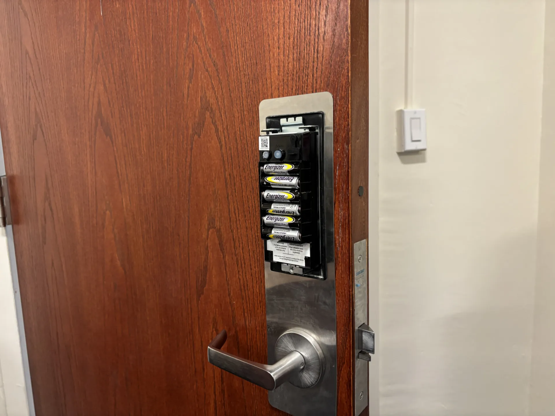 Partially open wooden door with an exposed electronic lock showing AA batteries.