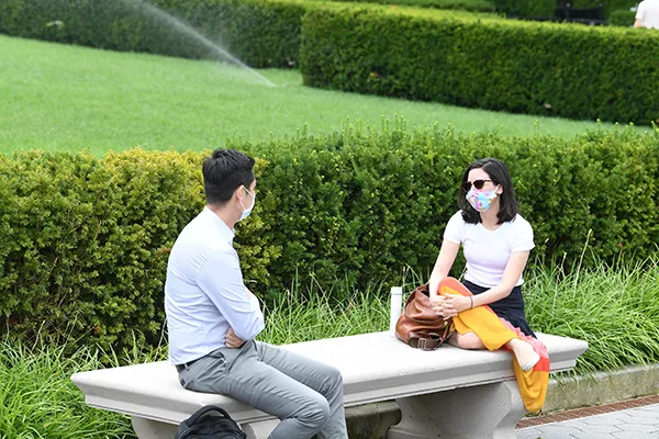 two students wearing masks sitting on bench chatting.